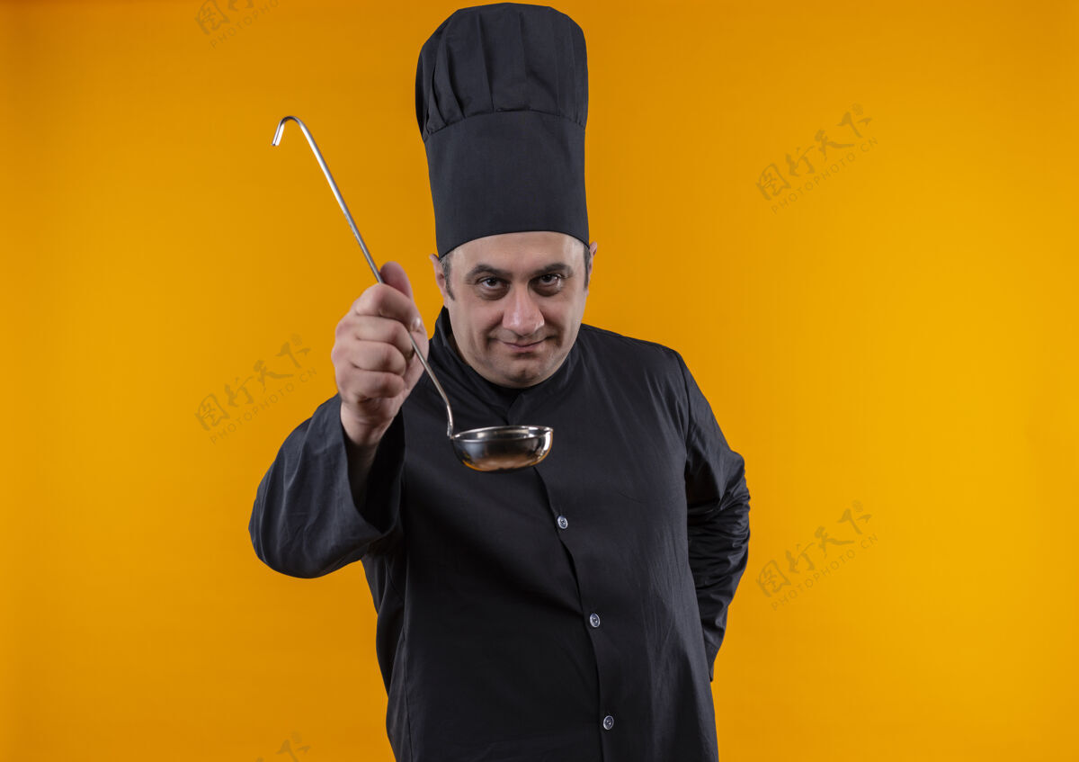 制服身着厨师制服的中年男厨师在黄色墙壁上拿着勺子 留有复制空间厨师中年看着