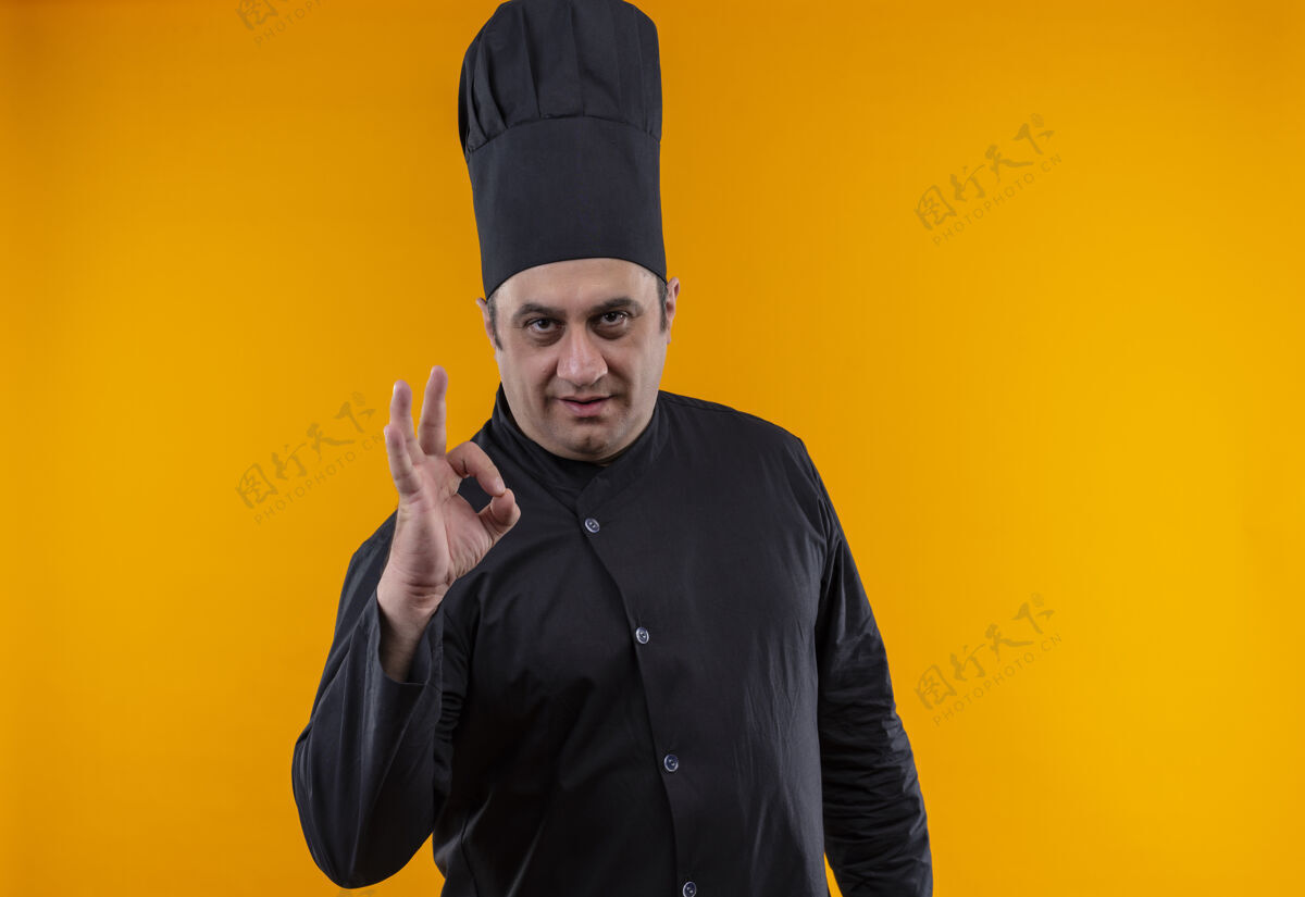 手势身着厨师制服的中年男厨师在黄色的墙壁上展示了一个很好的手势展示厨师厨师