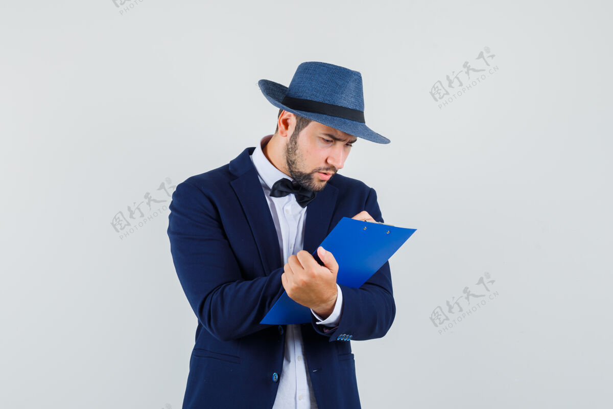 手年轻人穿着西装 戴着帽子 忙着在剪贴板上做笔记正视图时尚采取西装