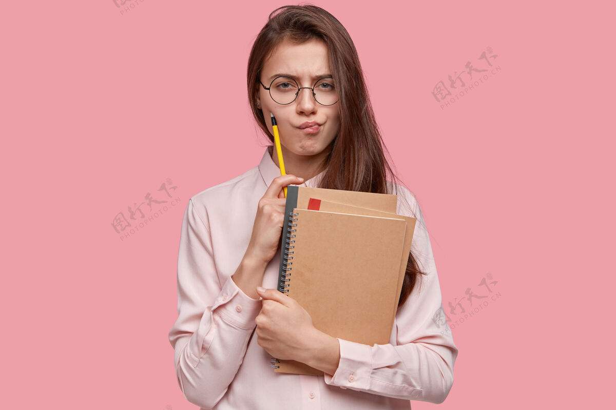 眼镜沮丧的黑发女人表情严肃 拿着铅笔和记事本 皱着眉头 想着写毕业论文笔记本个人严肃