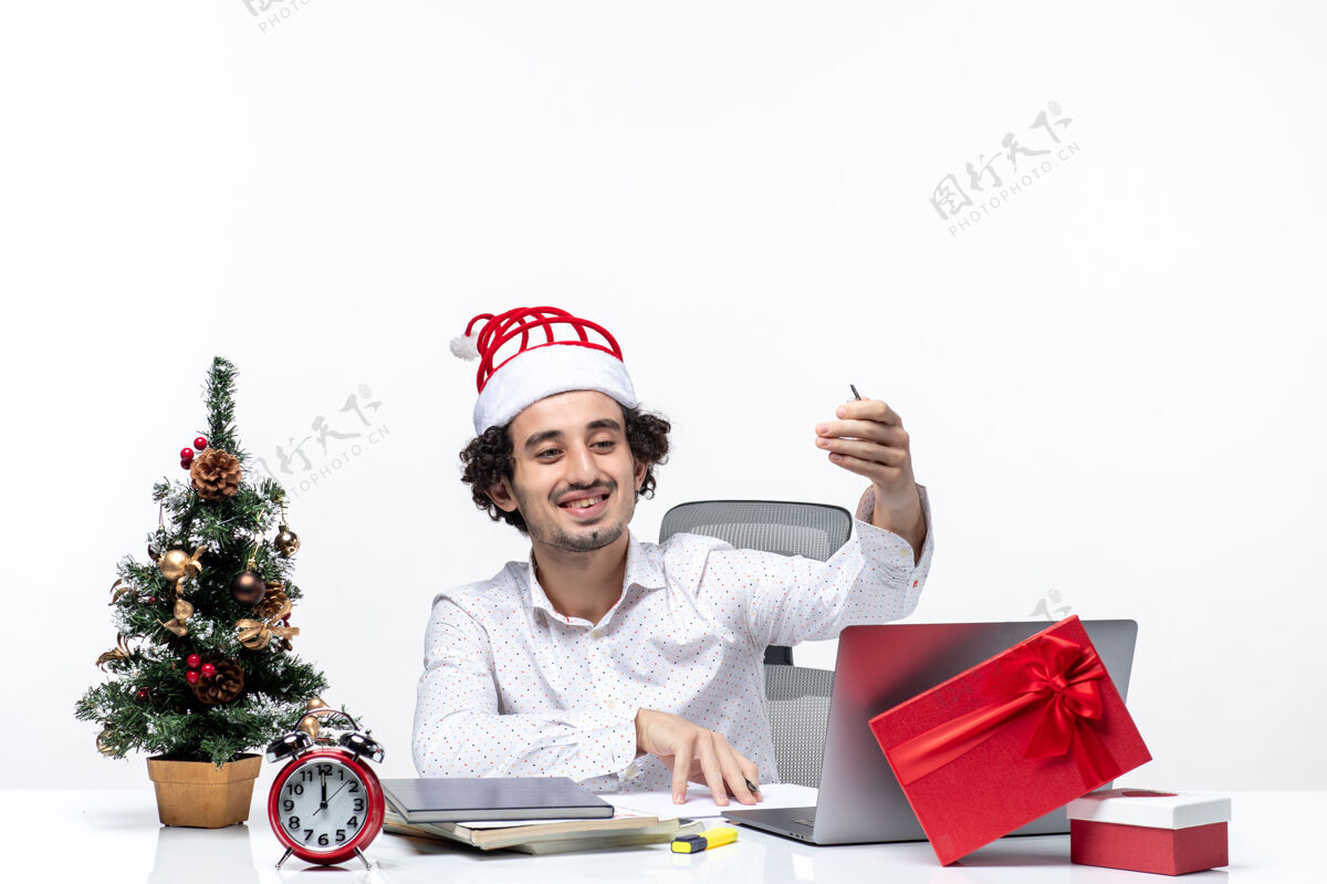 圣诞节满意的年轻商人与有趣的圣诞老人帽子检查书写笔记和庆祝圣诞节在白色背景的办公室圣诞老人帽子检查