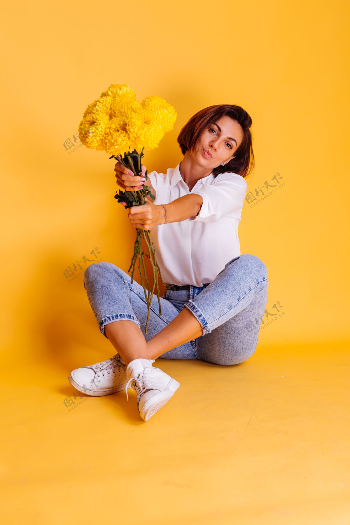 积极摄影棚拍摄的黄色背景快乐的白人妇女短发穿着休闲服白衬衫和牛仔裤手持一束黄色紫苑期待惊喜植物