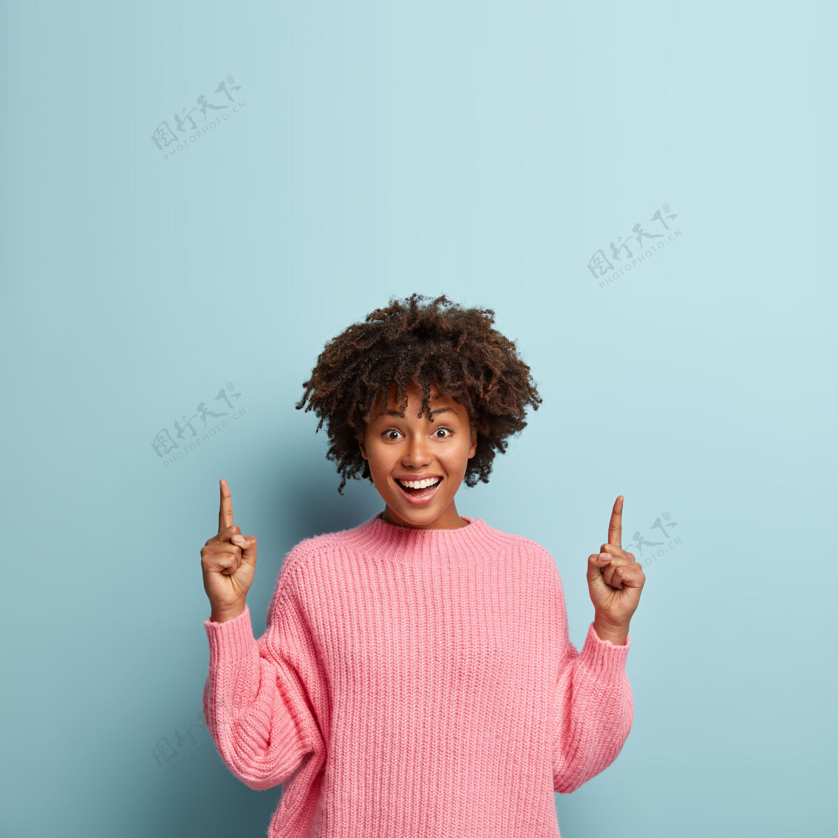 凝视积极的女卖家把两个前指向上指 露出牙齿般的微笑 穿着休闲的粉色套头衫指示向上爽快