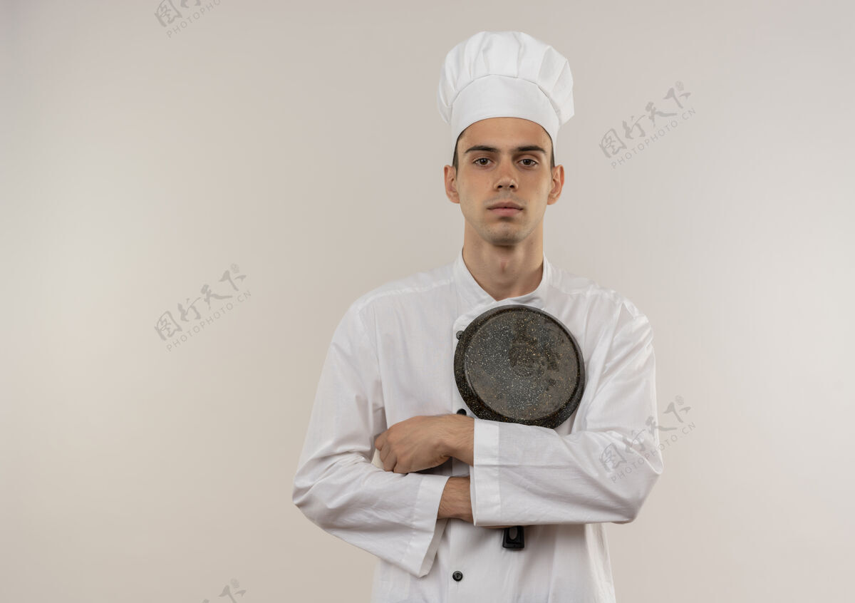 制服自信的年轻男厨师穿着厨师制服 双手交叉 手拿煎锅 站在隔离的白色墙壁上 有复制空间厨师拿着平底锅