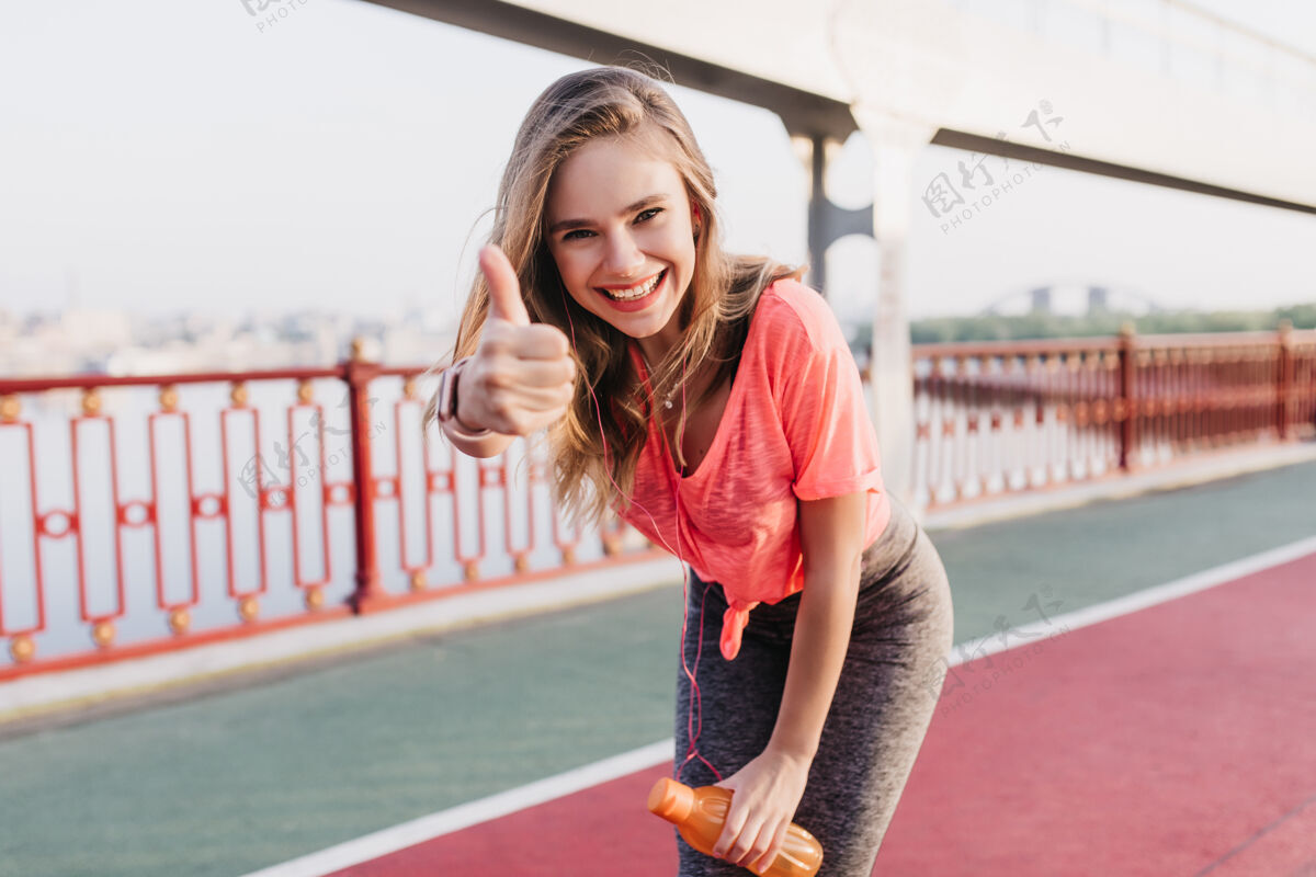 女人迷人的女跑步者摆出竖起大拇指的姿势可爱的白人女孩享受晨练的肖像体育场健康年轻