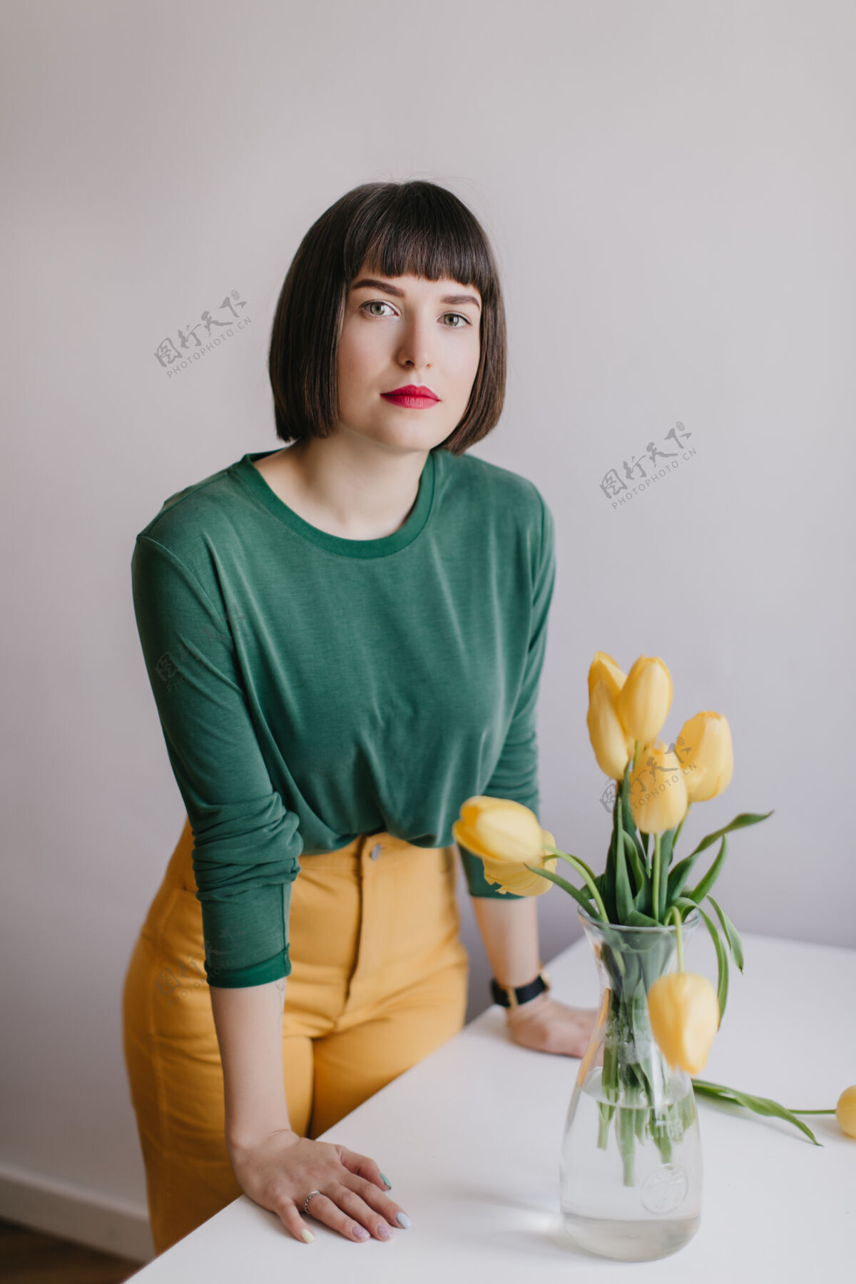 美丽严肃的女孩 带着时髦的妆容 站在桌旁 桌上摆着鲜花有兴趣的白人女模特在黄色郁金香旁摆姿势休闲时尚享受