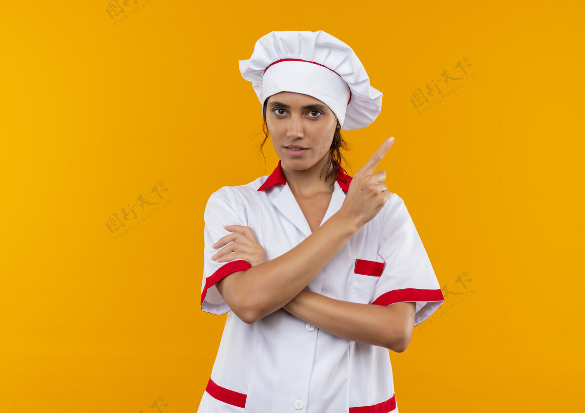 自信自信的年轻女厨师穿着厨师制服 指着旁边隔离的黄色墙壁 留有临摹空间厨师女制服
