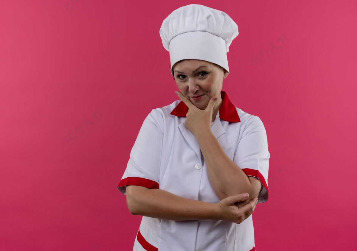 下巴身着厨师制服的中年女厨师高兴地把手放在隔离的粉红色墙壁上的下巴上 墙上留有临摹空间放厨师女