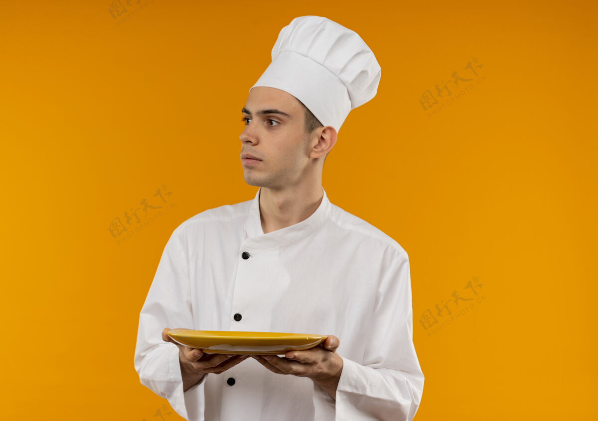 盘子望着旁边年轻的男酷穿着厨师制服的托板 在隔离的黄色墙壁上留有临摹的空间男酷戴着