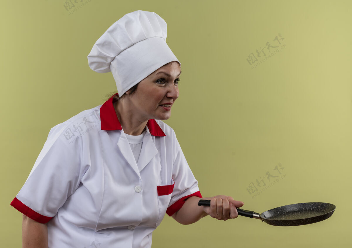 厨师看着旁边穿着厨师制服的中年女厨师手拿煎锅站在隔离的绿墙上中年平底锅煎炸
